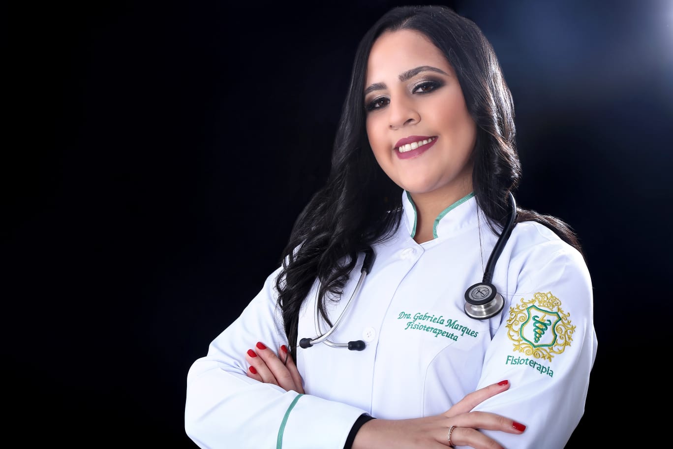 Gabriela Marques, fisioterapeuta, sorrindo de braços cruzados com jaleco e estetoscópio